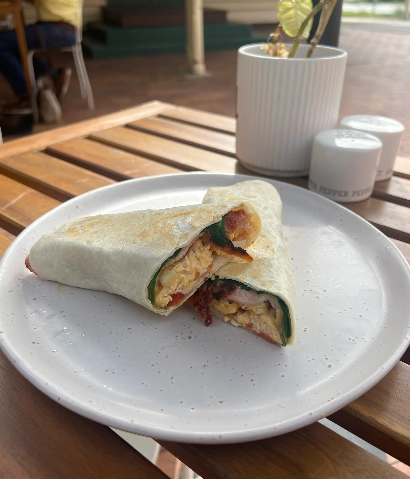 Hygge Cafe breakfast wrap cut in half revealing scrambled egg, bacon and spinach filling on a white plate