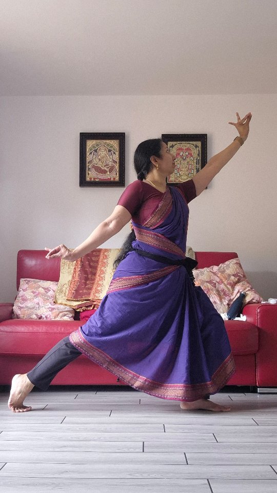 Dancer in rich purple silk saree with red border performing Bharatanatyam pose indoors