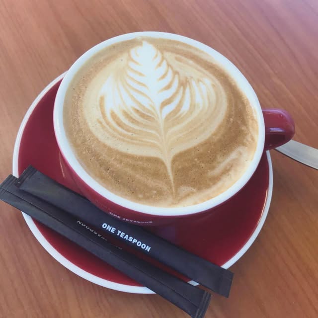 A latte art coffee in a red cup on a timber cafe table