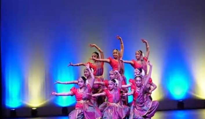 Group performance of young dancers in mauve-purple costumes under coloured stage lighting
