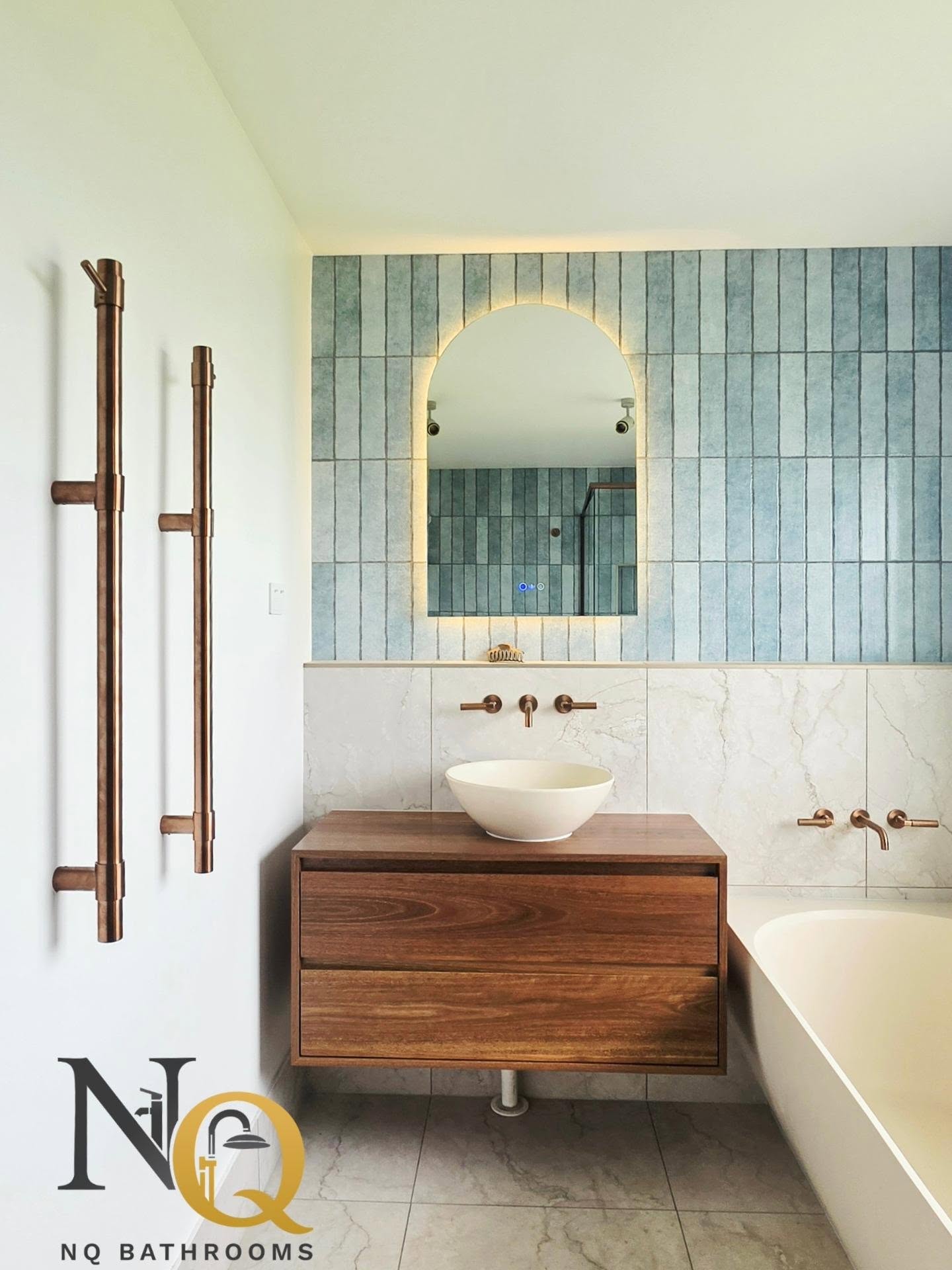 Bathroom vanity area with teal subway tiles and arched backlit mirror