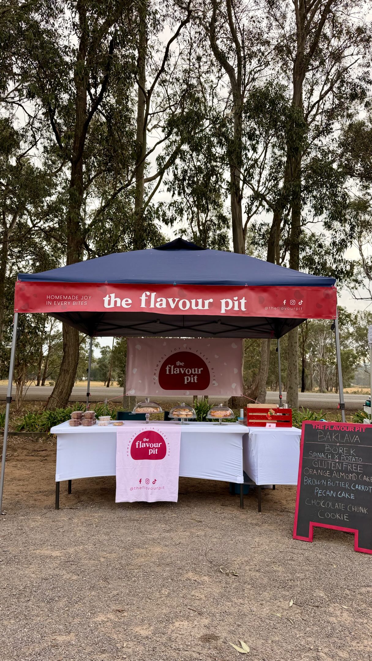 The Flavour Pit stall table laid out with cake stands and treats under a marquee among trees