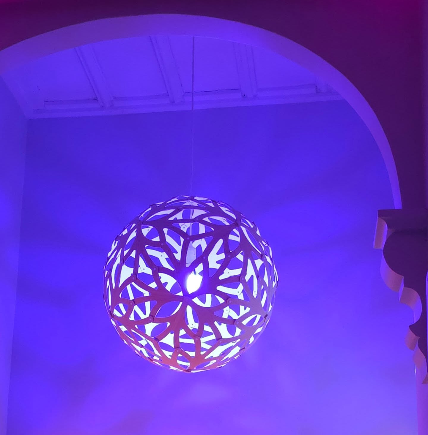 Patterned pendant lamp glowing in soft violet light under an arched ceiling