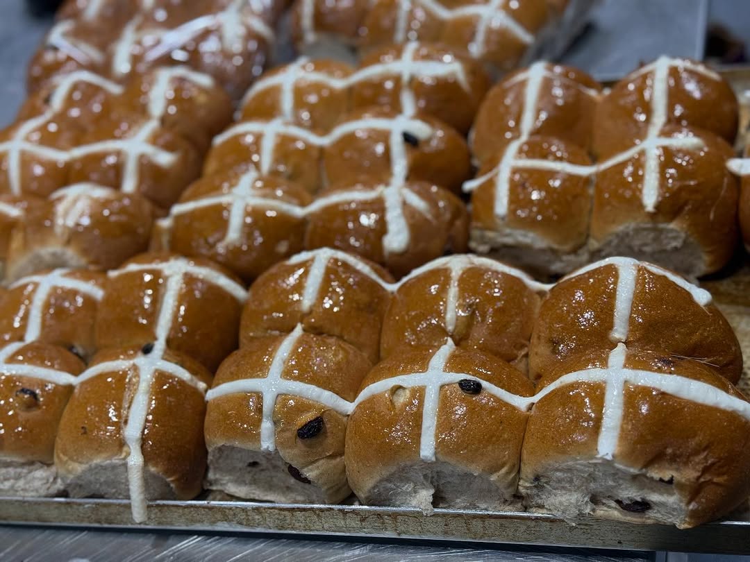 Fresh hot cross buns in rows on a cooling rack, glazed and topped with a white icing cross