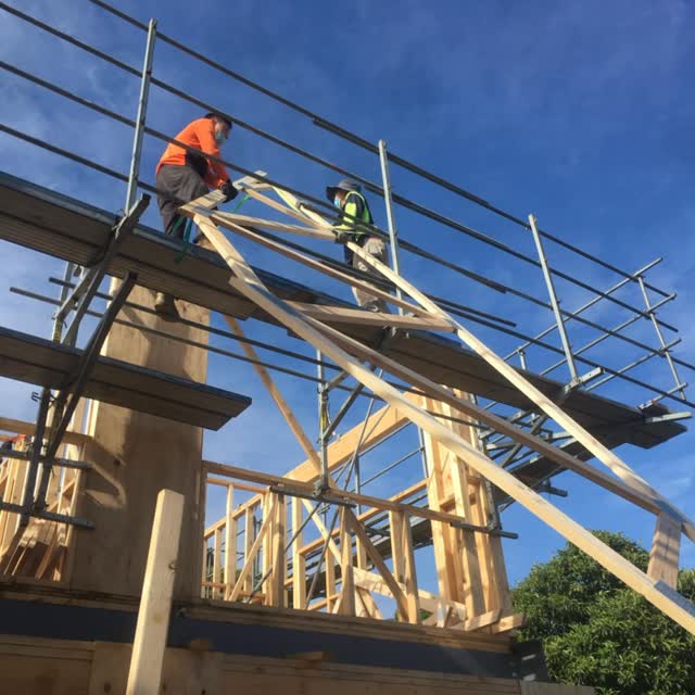 Tekcon Constructions builders working on the timber roof frame of a new home under a clear blue sky