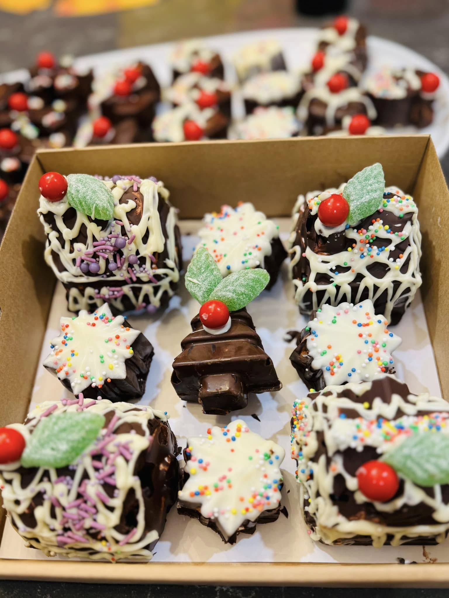 A cardboard box of decorated chocolate slices and white chocolate toppers