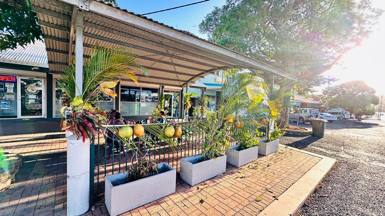 Outdoor dining verandah at Island Rooster Uncle Frankie's Cafe with tropical plants, seating and warm afternoon sunlight