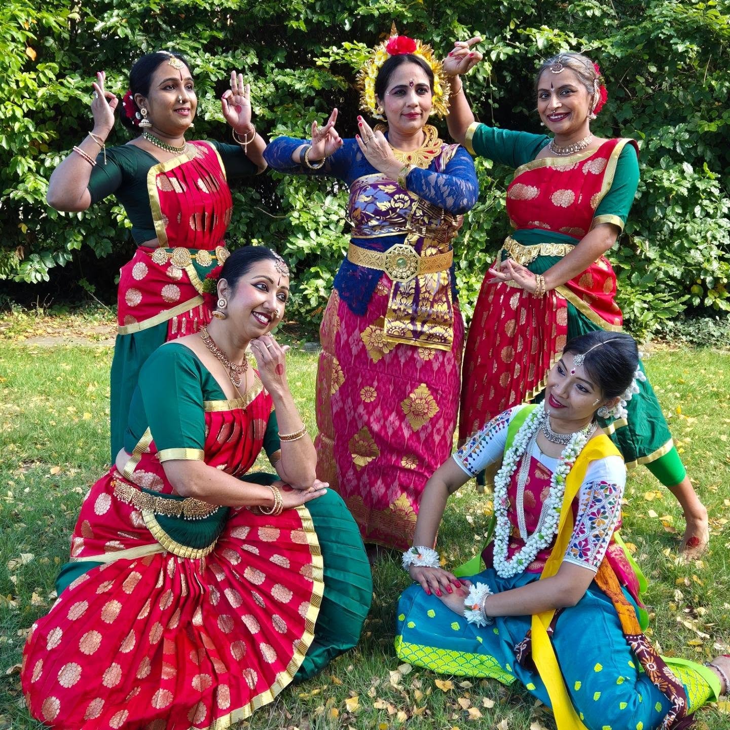 Group of adult dancers in vibrant red silk sarees with gold trim posing outdoors