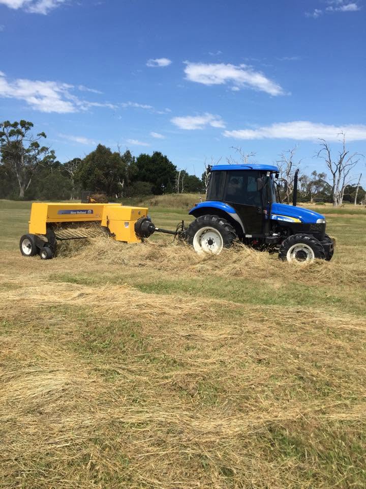 Blue New Holland tractor with yellow New Holland hay baler working through dry cut grass on a Mornington Peninsula farm