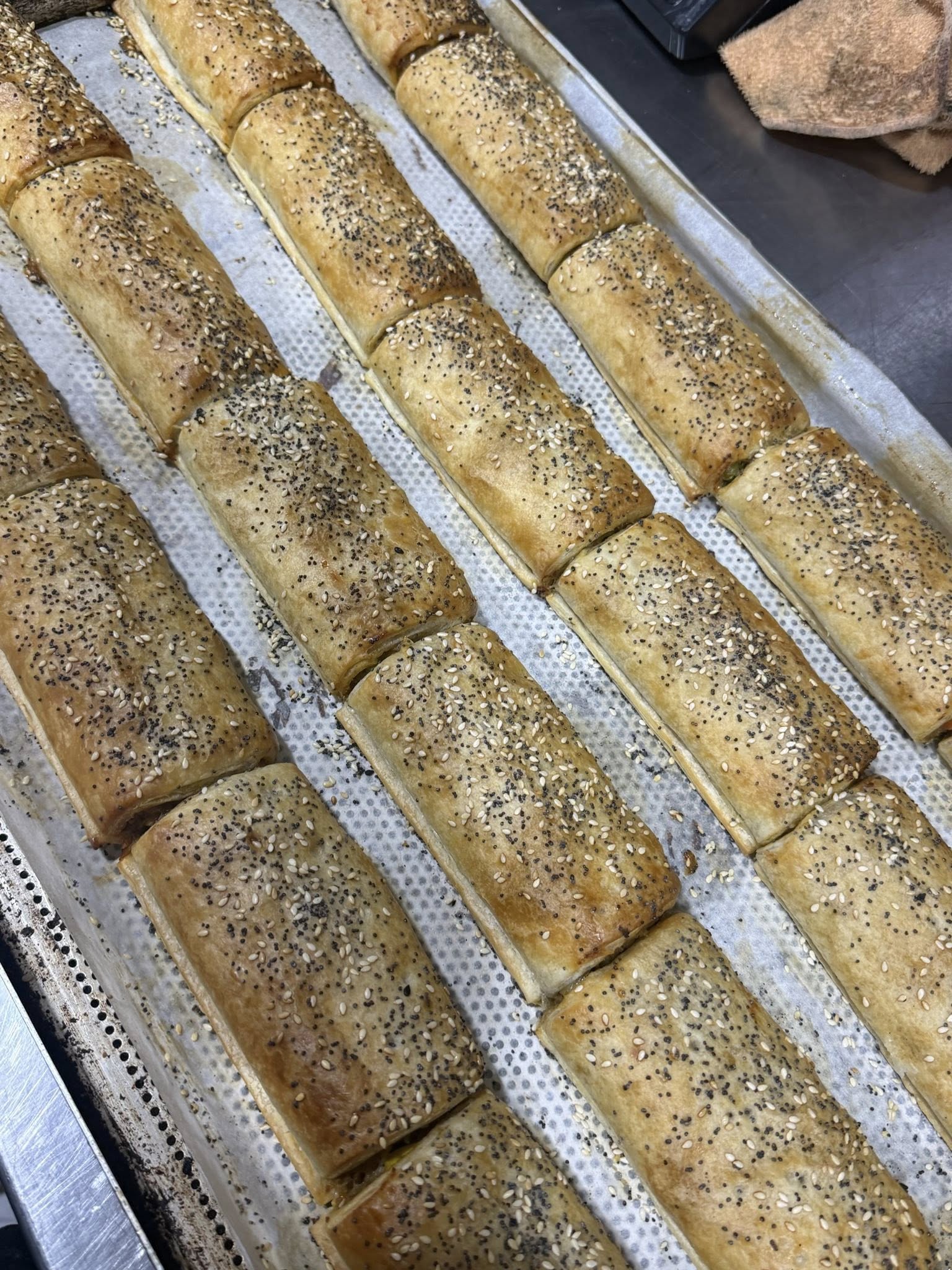 Rows of freshly baked seeded sausage rolls cooling on a commercial baking tray
