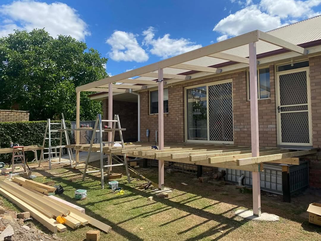 Deck and pergola frame under construction against a brick house