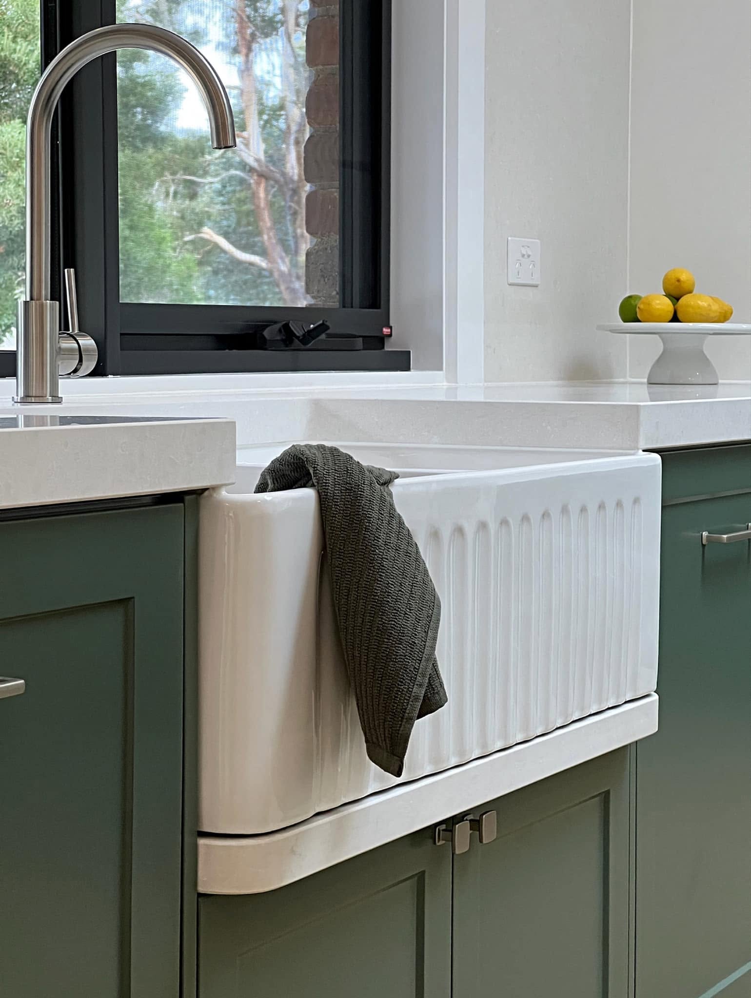 Spotlessly cleaned farmhouse kitchen sink with green cabinetry in a New Gisborne home