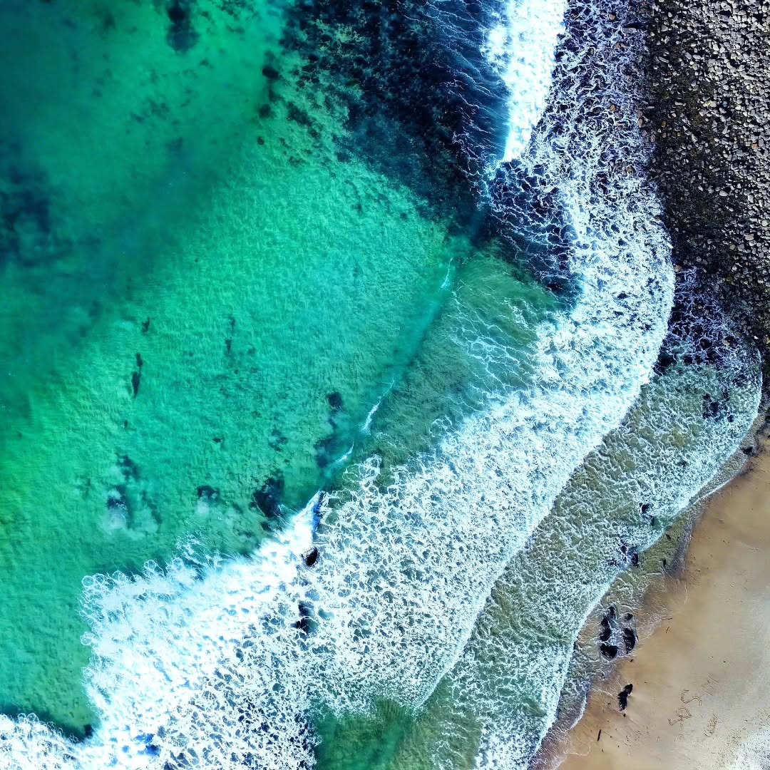 Aerial close-up of teal ocean water washing over a rocky shoreline
