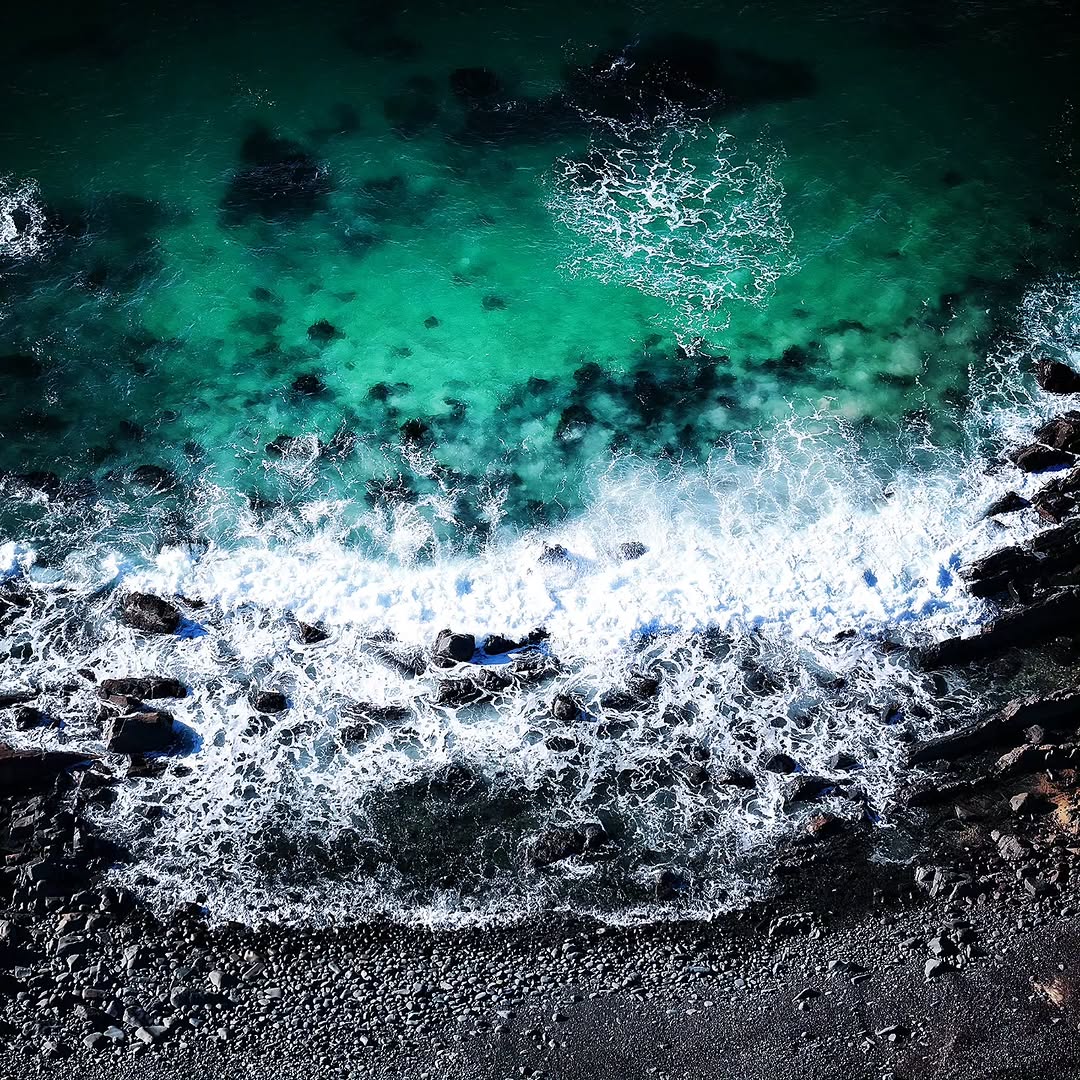 Aerial detail of green-toned surf breaking over a rocky point