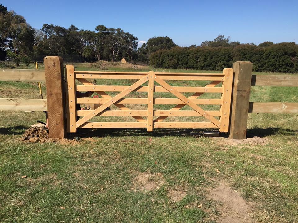 Freshly installed five-bar timber farm gate between hardwood posts on a sunny green paddock