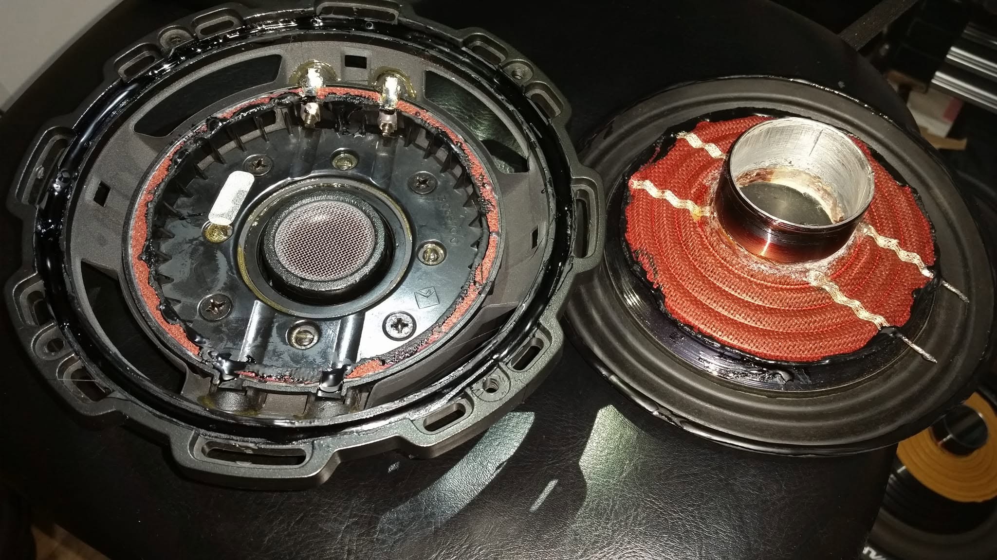 Two halves of a car subwoofer laid out on a black workbench