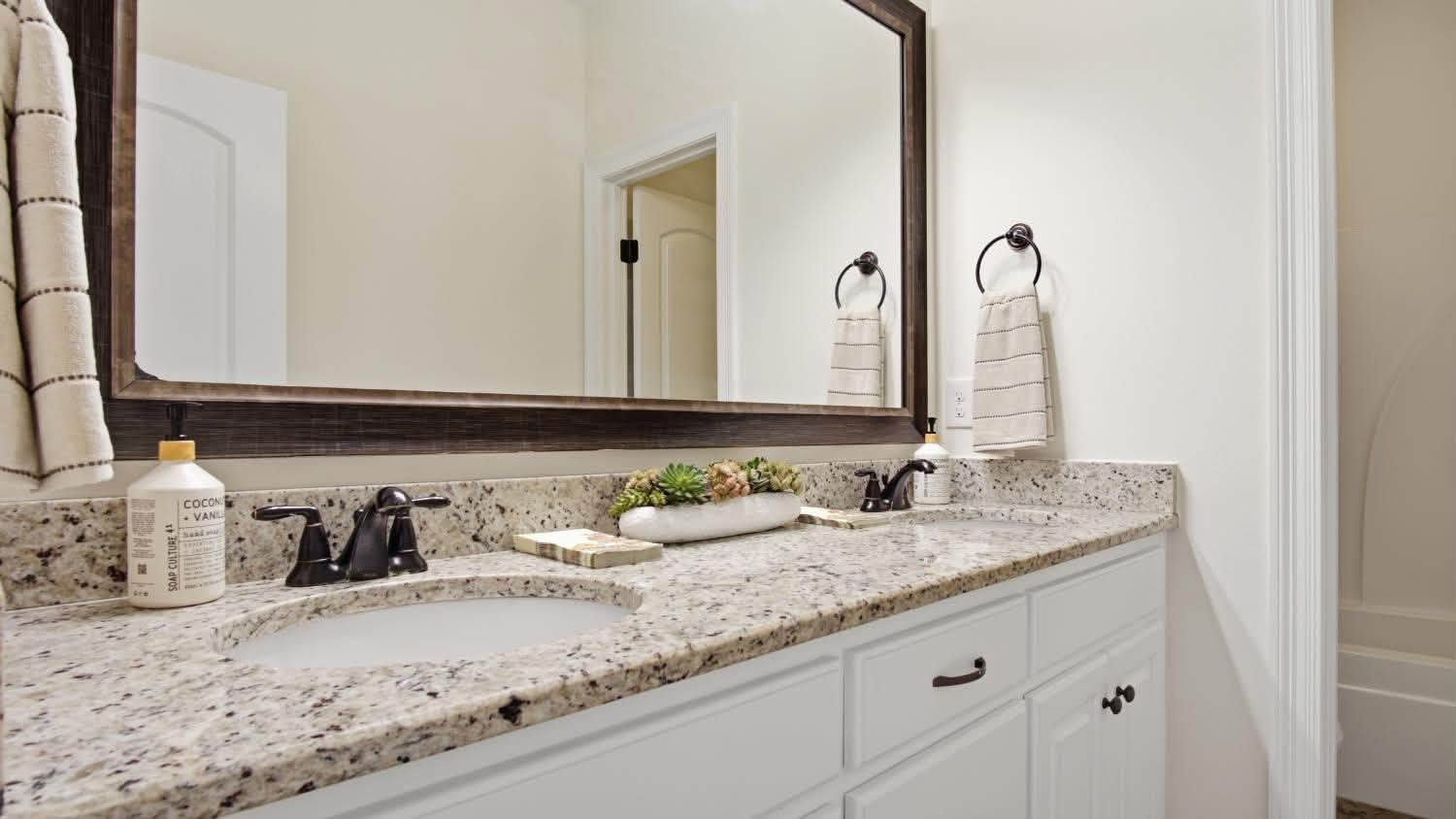 A bathroom vanity with double sinks, granite benchtop and a large mirror