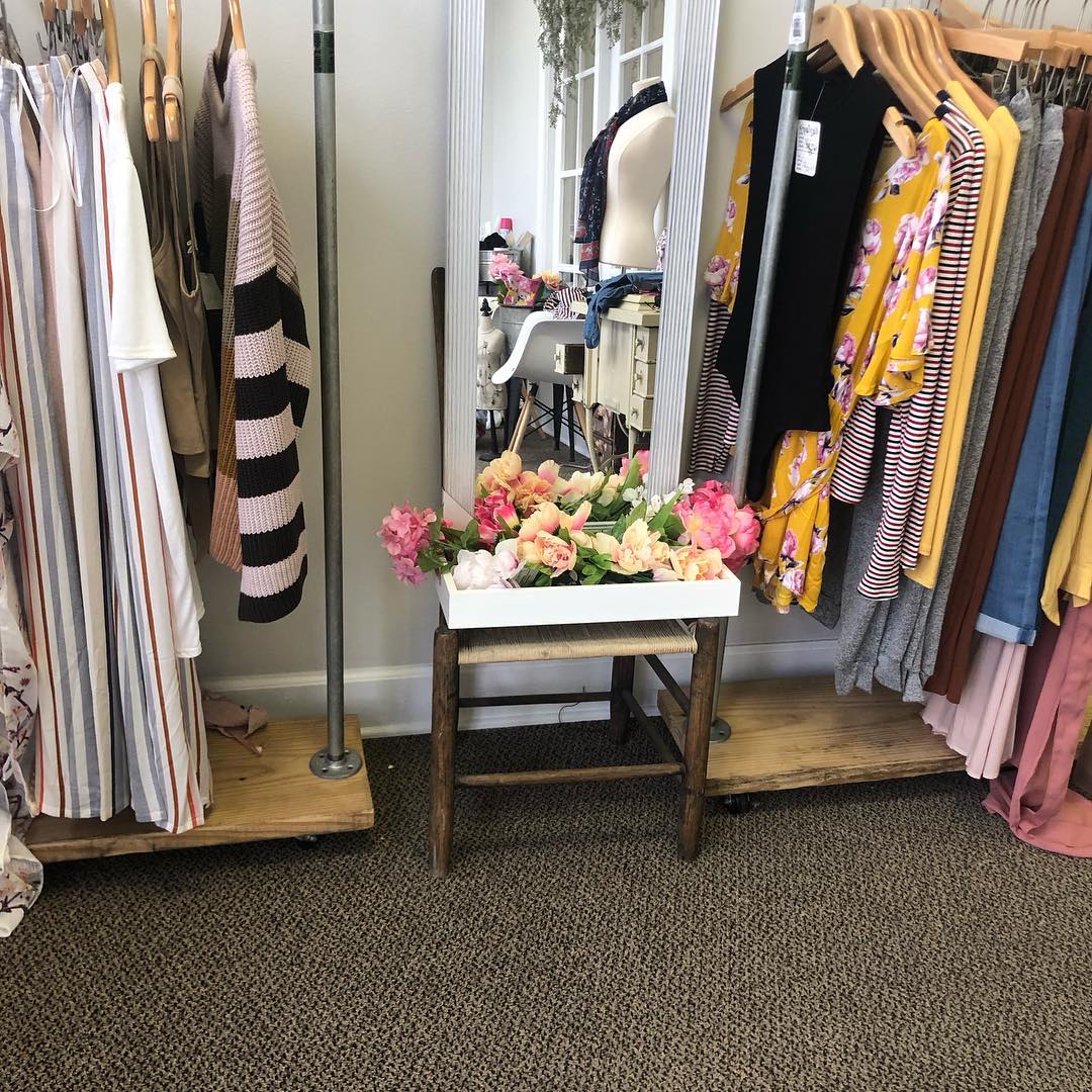 Clothing racks and a tray of pink and peach flowers inside Constance's Boutique