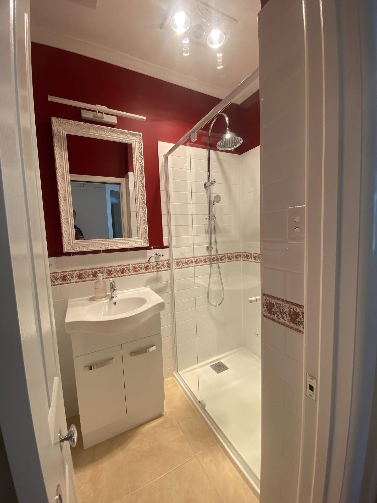 Completed bathroom renovation with red feature wall and shower