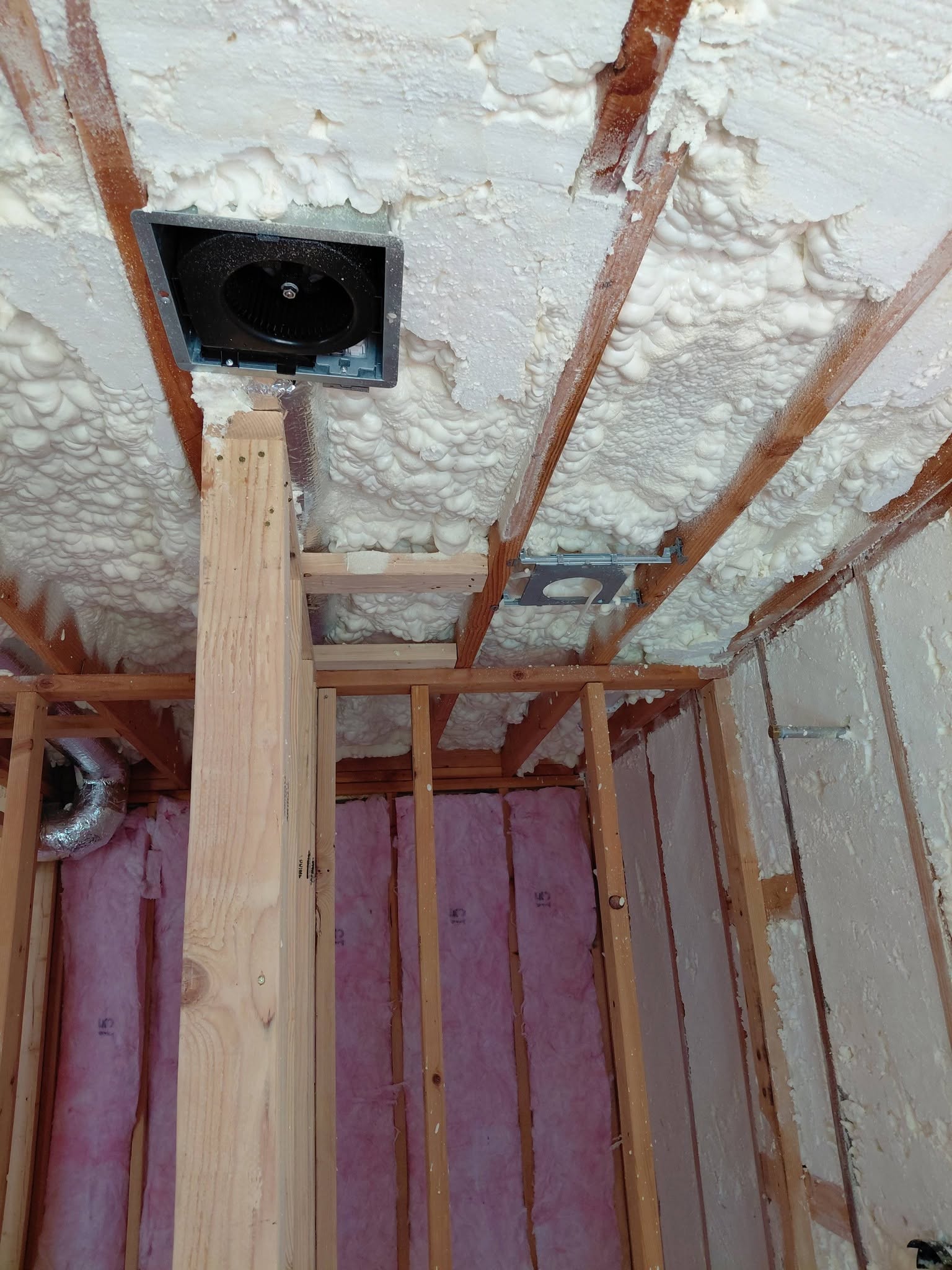 Exhaust fan mounted in spray-foam insulated ceiling inside timber framing