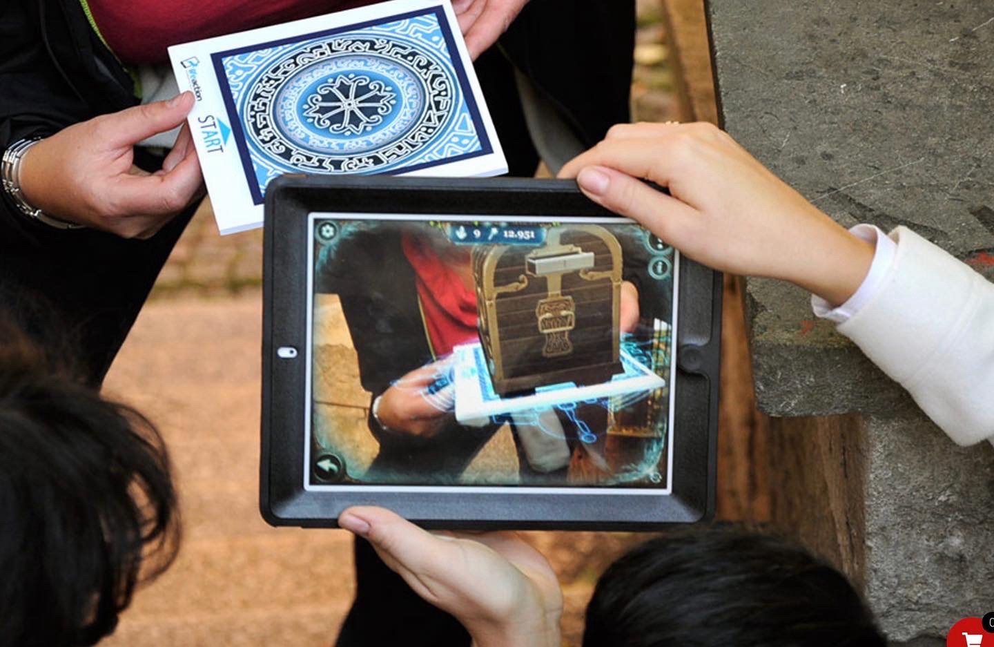 Gruppe schaut gemeinsam auf ein iPad, auf dem eine AR-Schatztruhe erscheint – Das Geheimnisvolle Portal Magdeburg