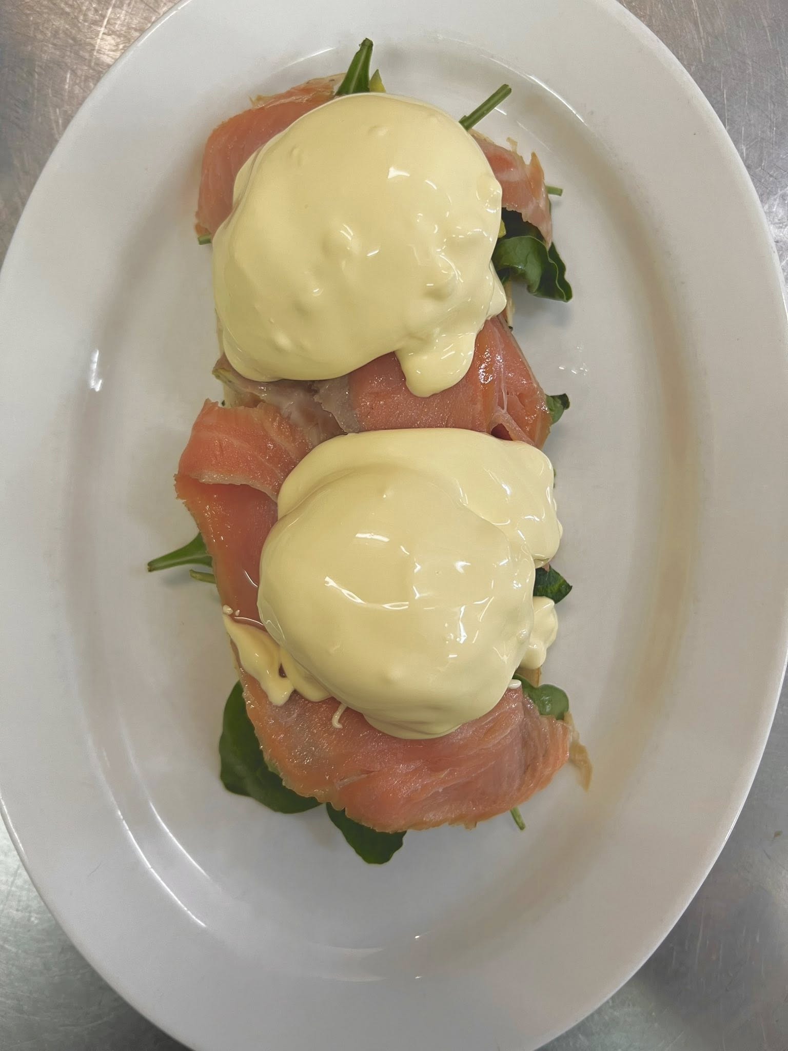 Smoked salmon eggs benedict with hollandaise on a white oval plate — a popular brunch choice at Cheryl-Lyn's Cafe
