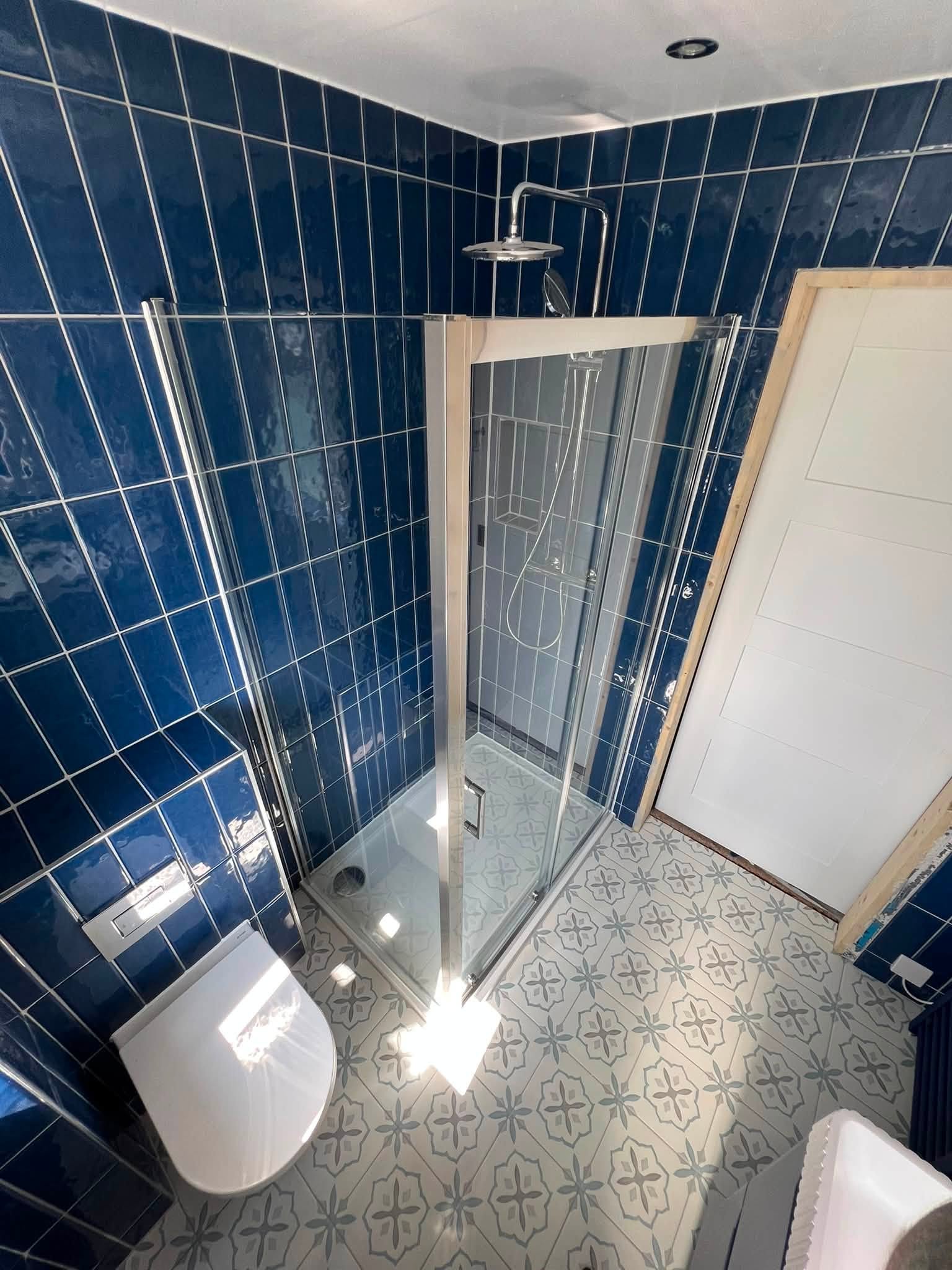 Glass shower enclosure with wall-hung toilet and patterned floor tiles