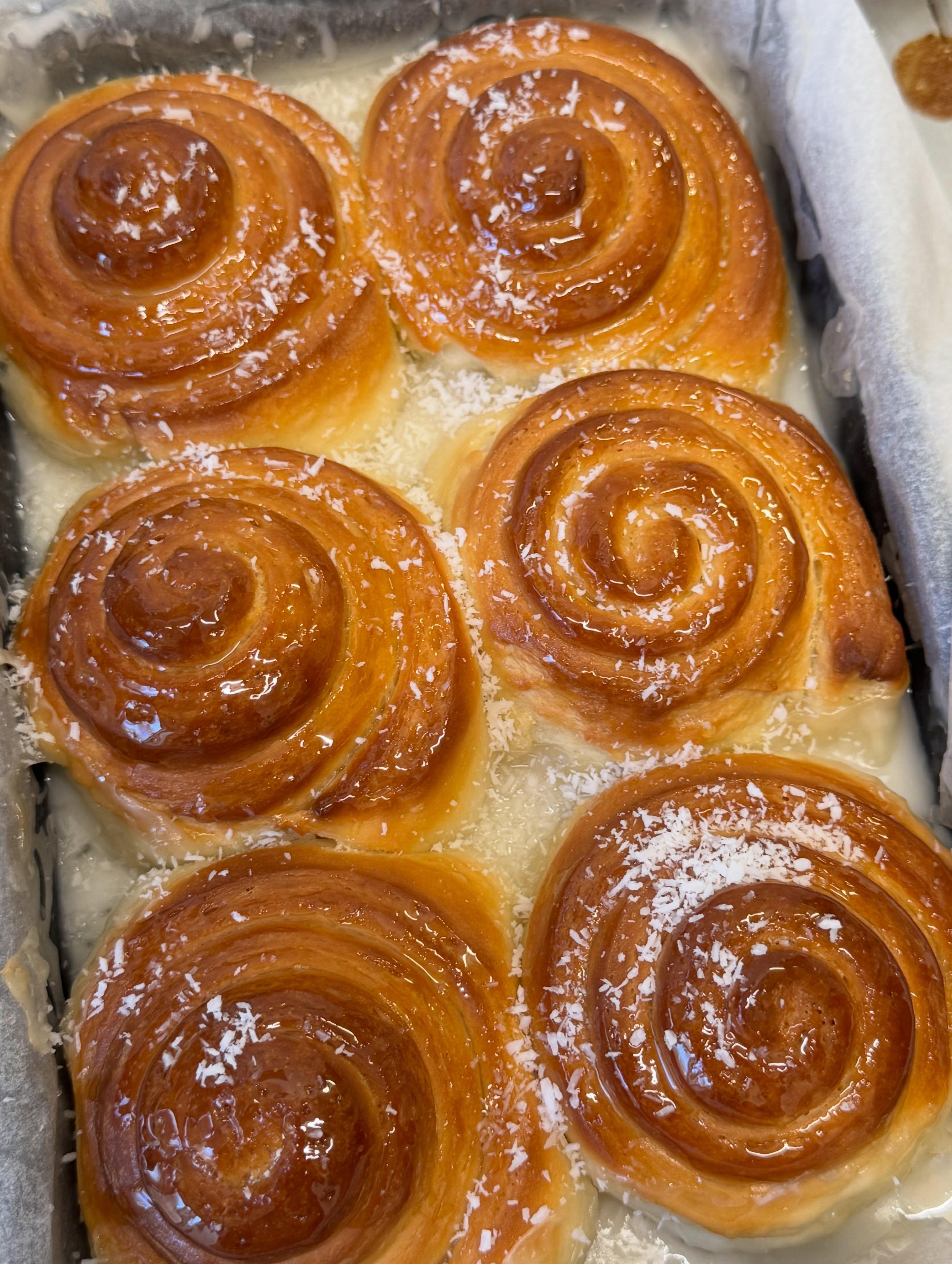 A tray of freshly baked golden glazed coconut cinnamon rolls straight from the oven at Lenaya Baked Goods