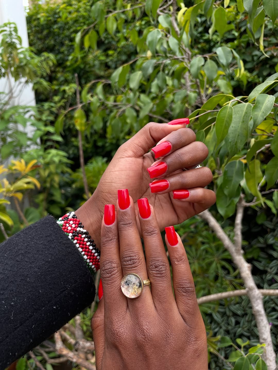 Vibrant red long nails against tropical green foliage