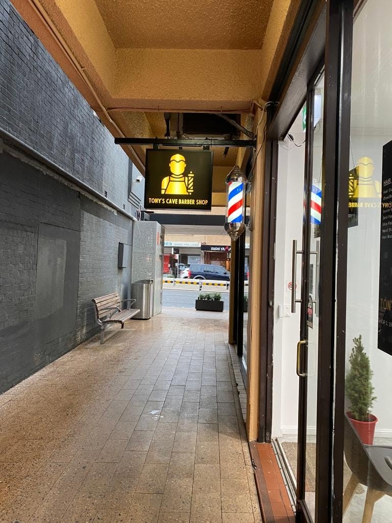 Tony's Cave Barber Shop alleyway exterior with illuminated signage and barber pole