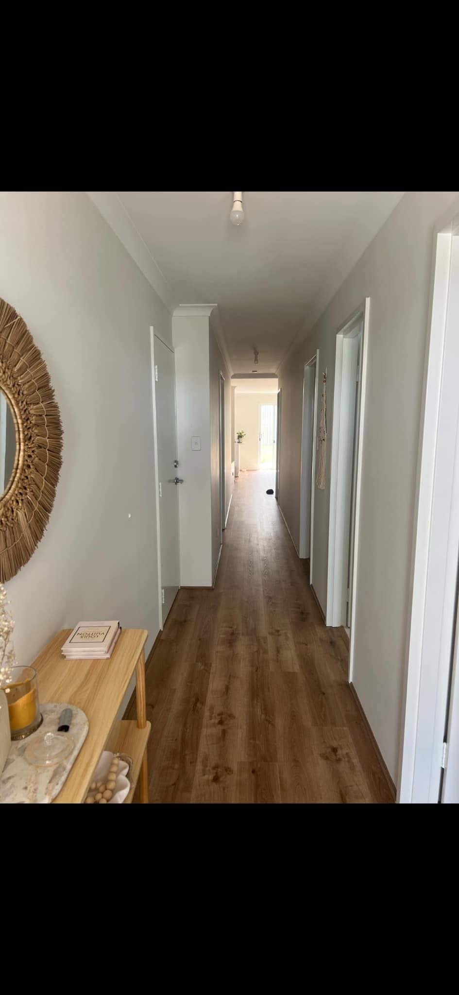 Freshly painted hallway with warm timber floors, wicker mirror and console table