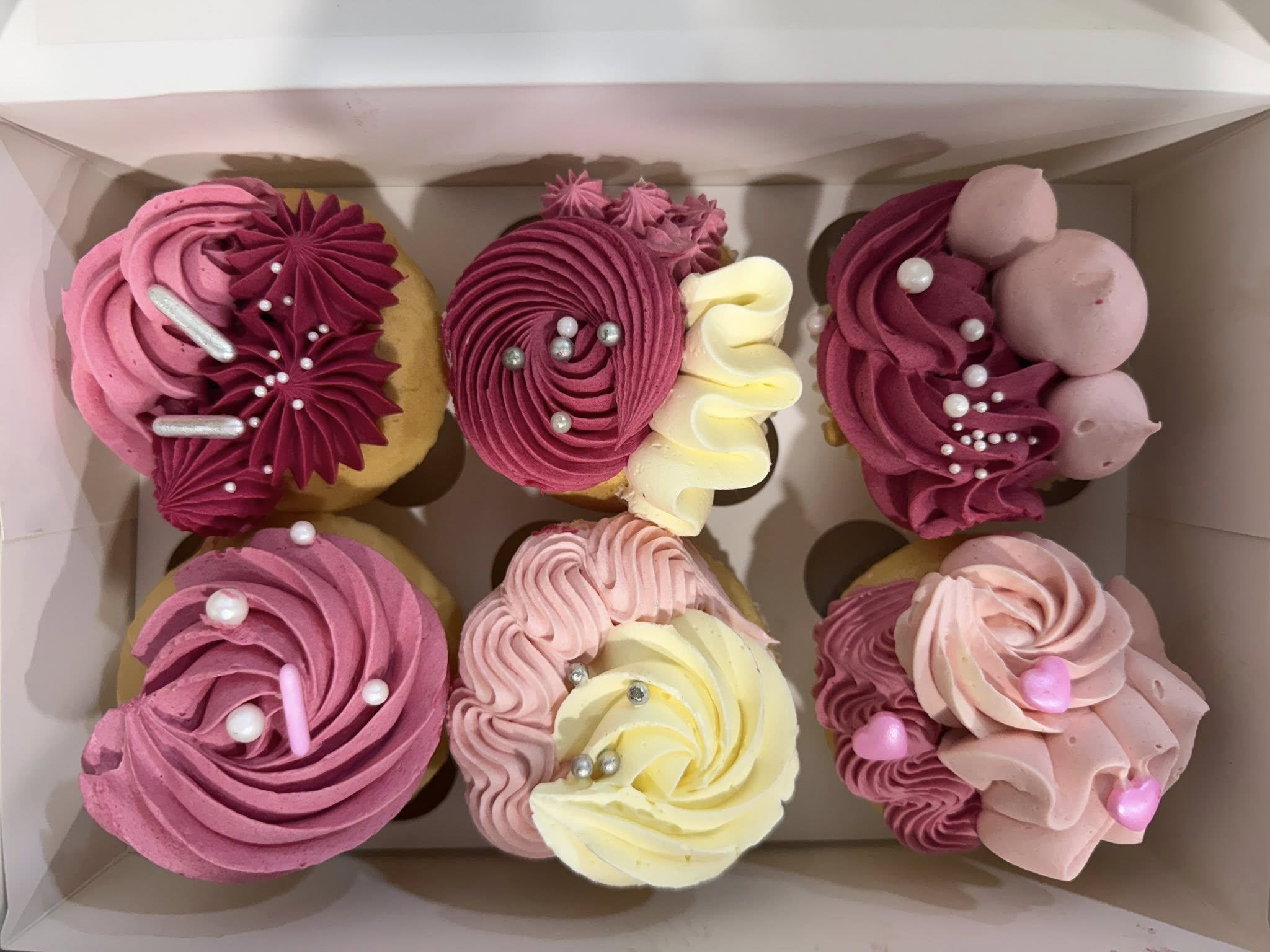 Six beautifully decorated cupcakes in shades of pink and cream with intricate piped buttercream swirls