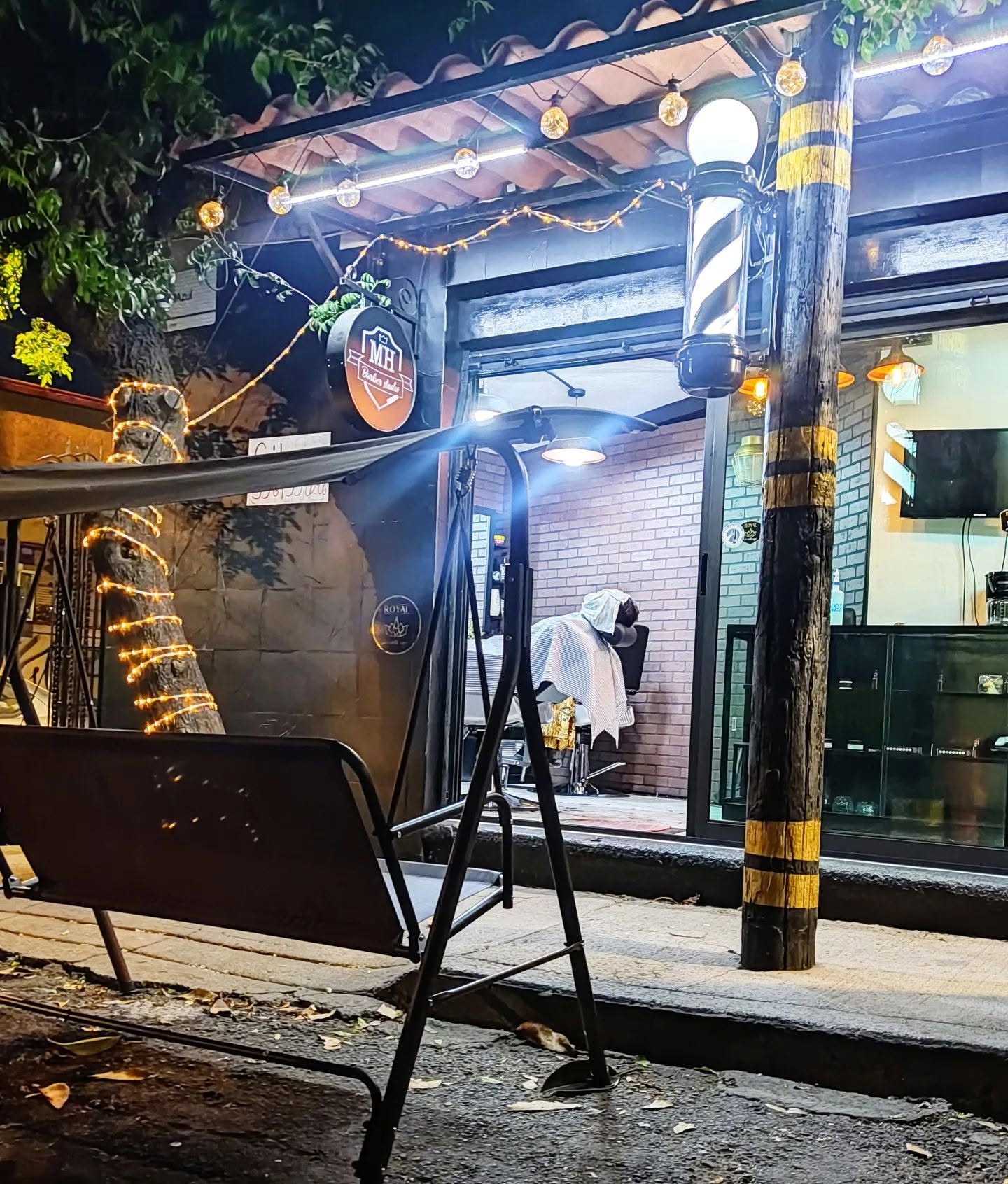 MH Barbers Studio exterior — barber pole and shopfront at night