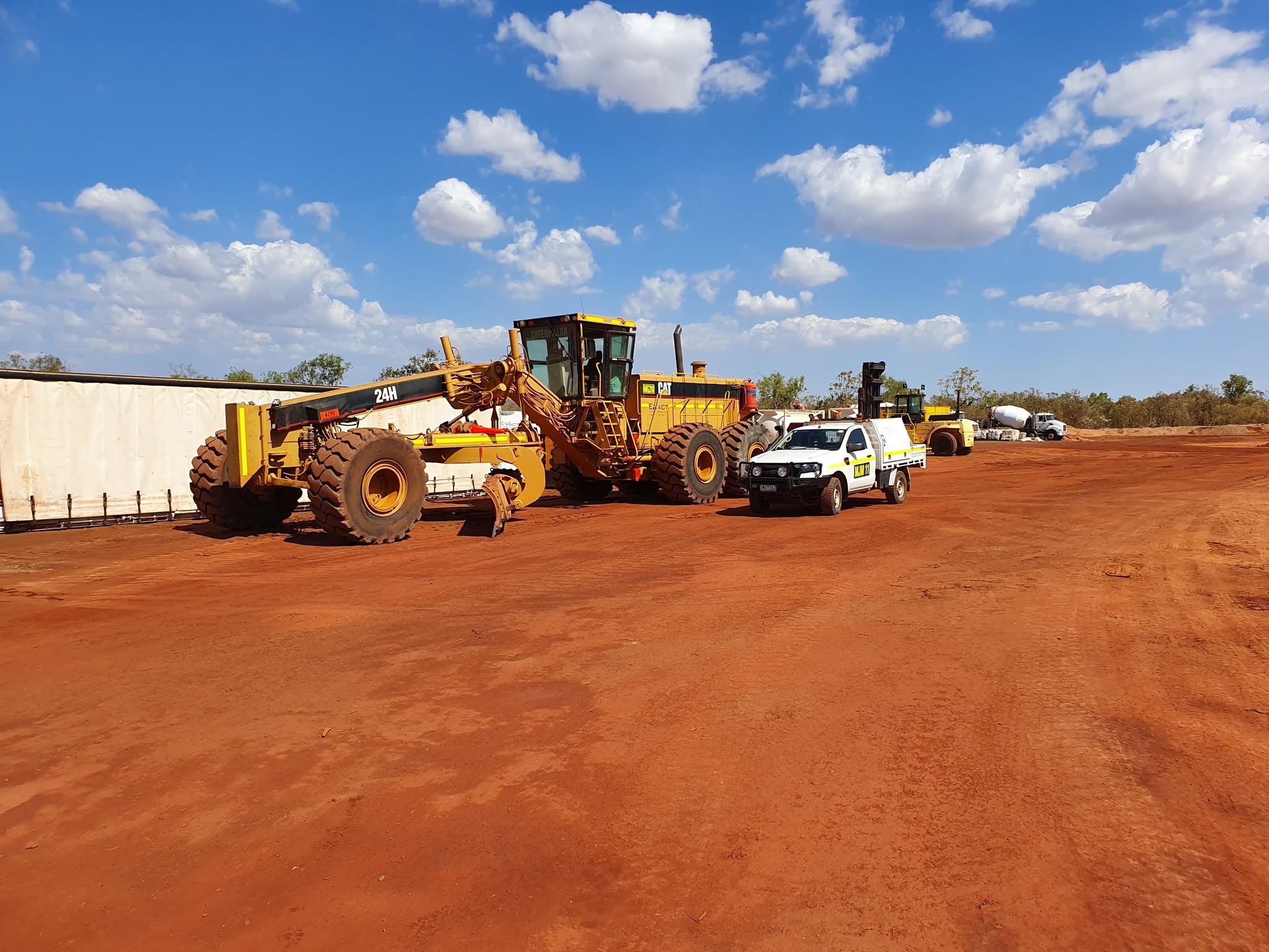 CAT motor grader and service ute on a red-dirt construction site — mobile heavy equipment servicing