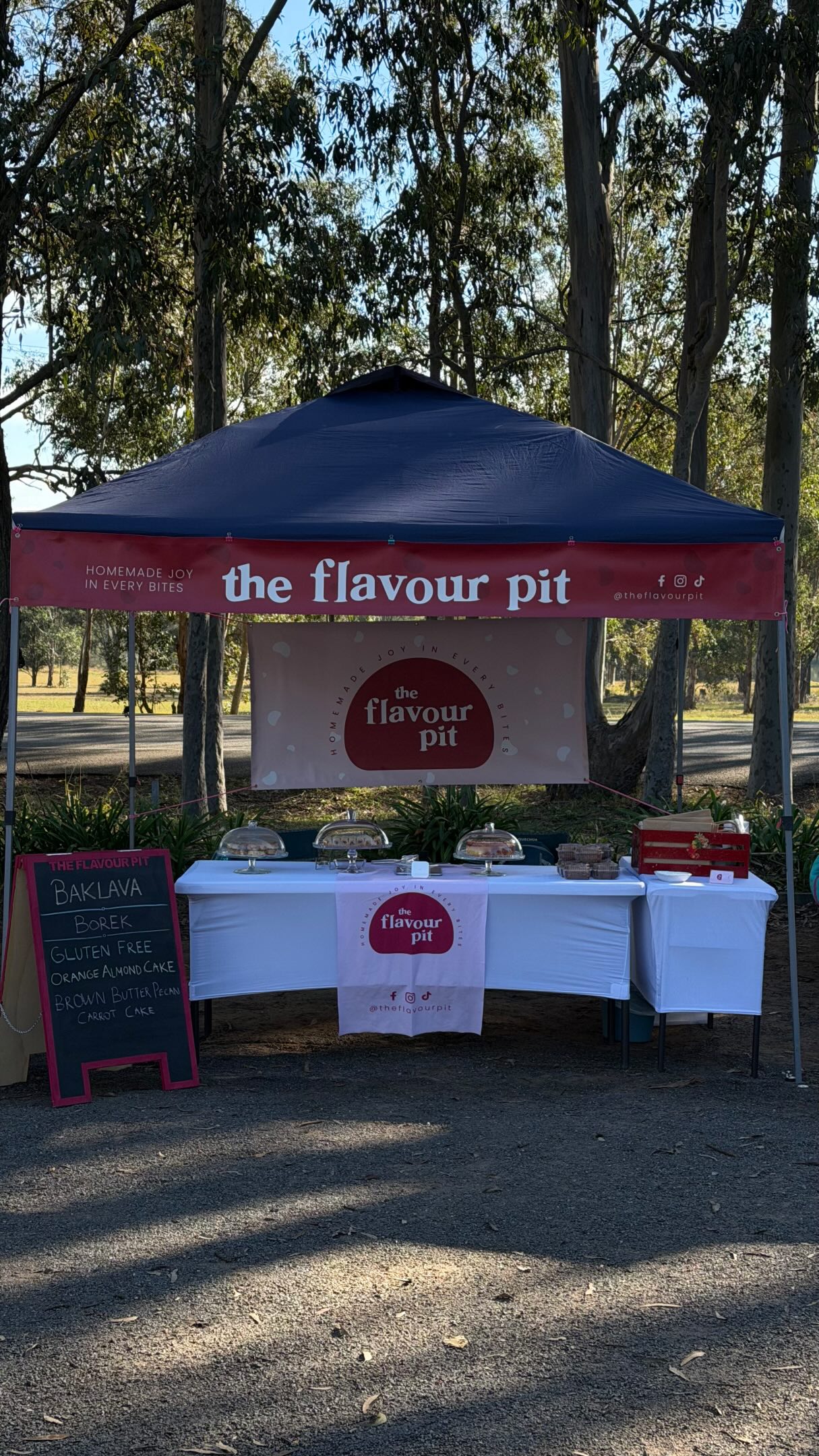 The Flavour Pit market stall set up under a marquee, displaying handmade cakes and treats