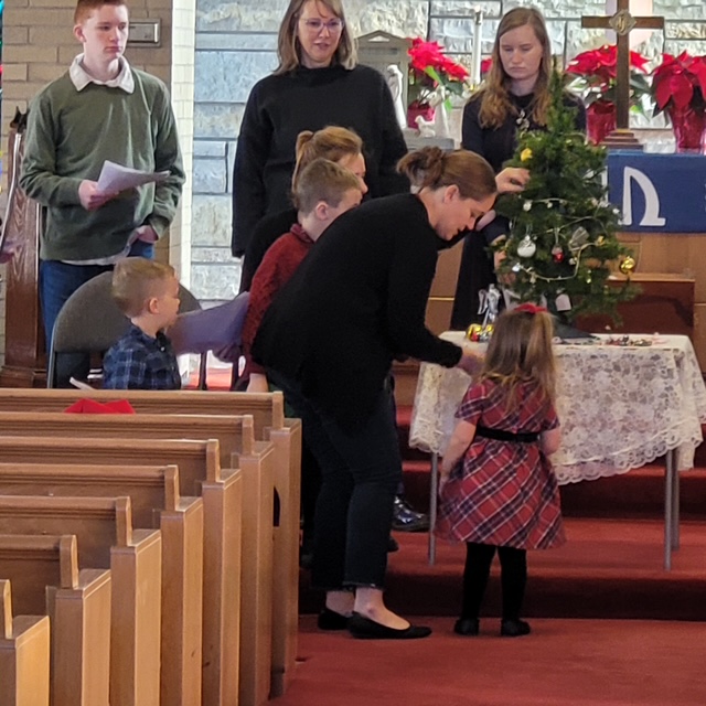 Families gathered near the altar to decorate the Christmas tree during a holiday service