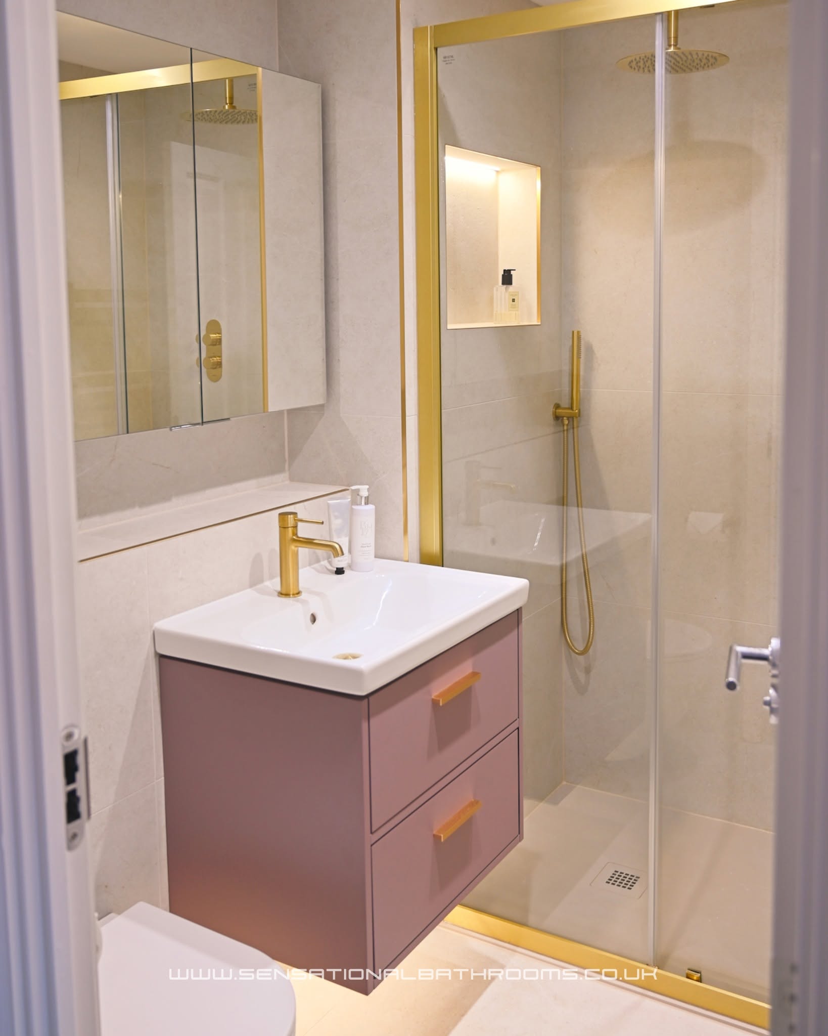Elegant bathroom with floating dusky pink vanity, gold fixtures, and walk-in glass shower