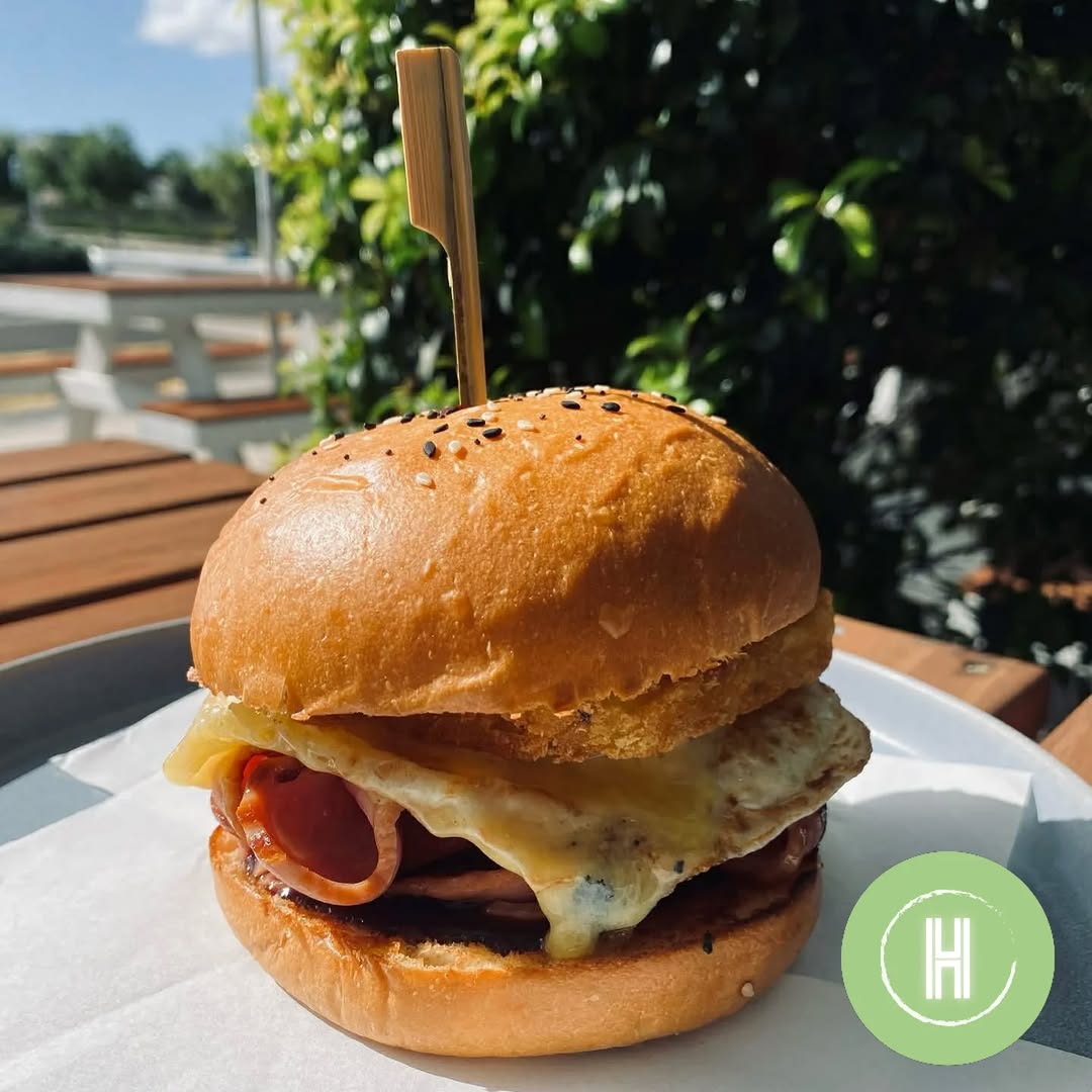 Golden sesame bun breakfast burger with egg, bacon and cheese on a white plate