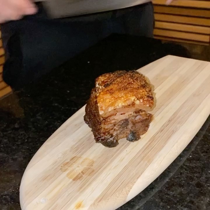 Crispy-skin pork belly resting on a bamboo board