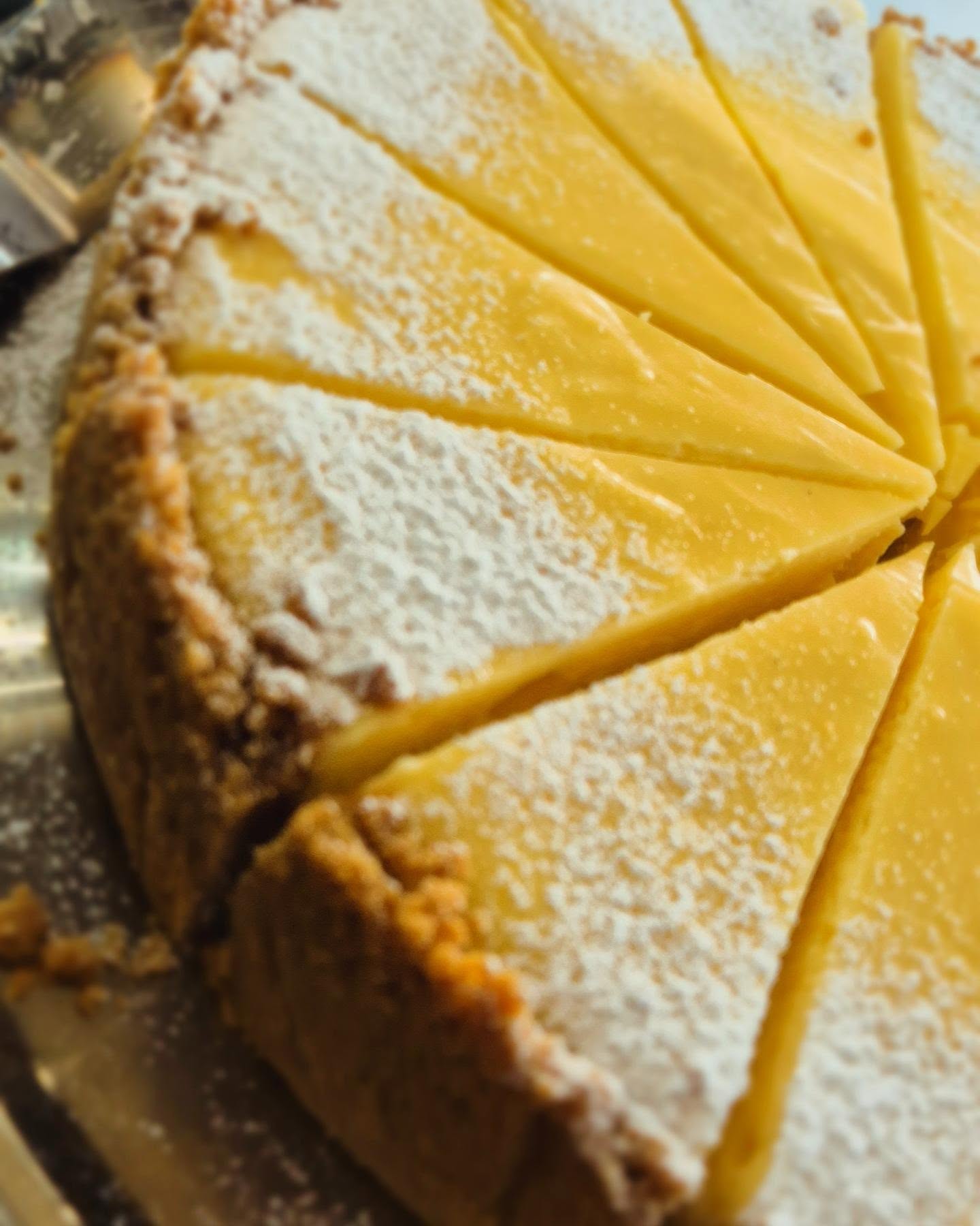 A lemon tart dusted with icing sugar, sliced and ready to serve
