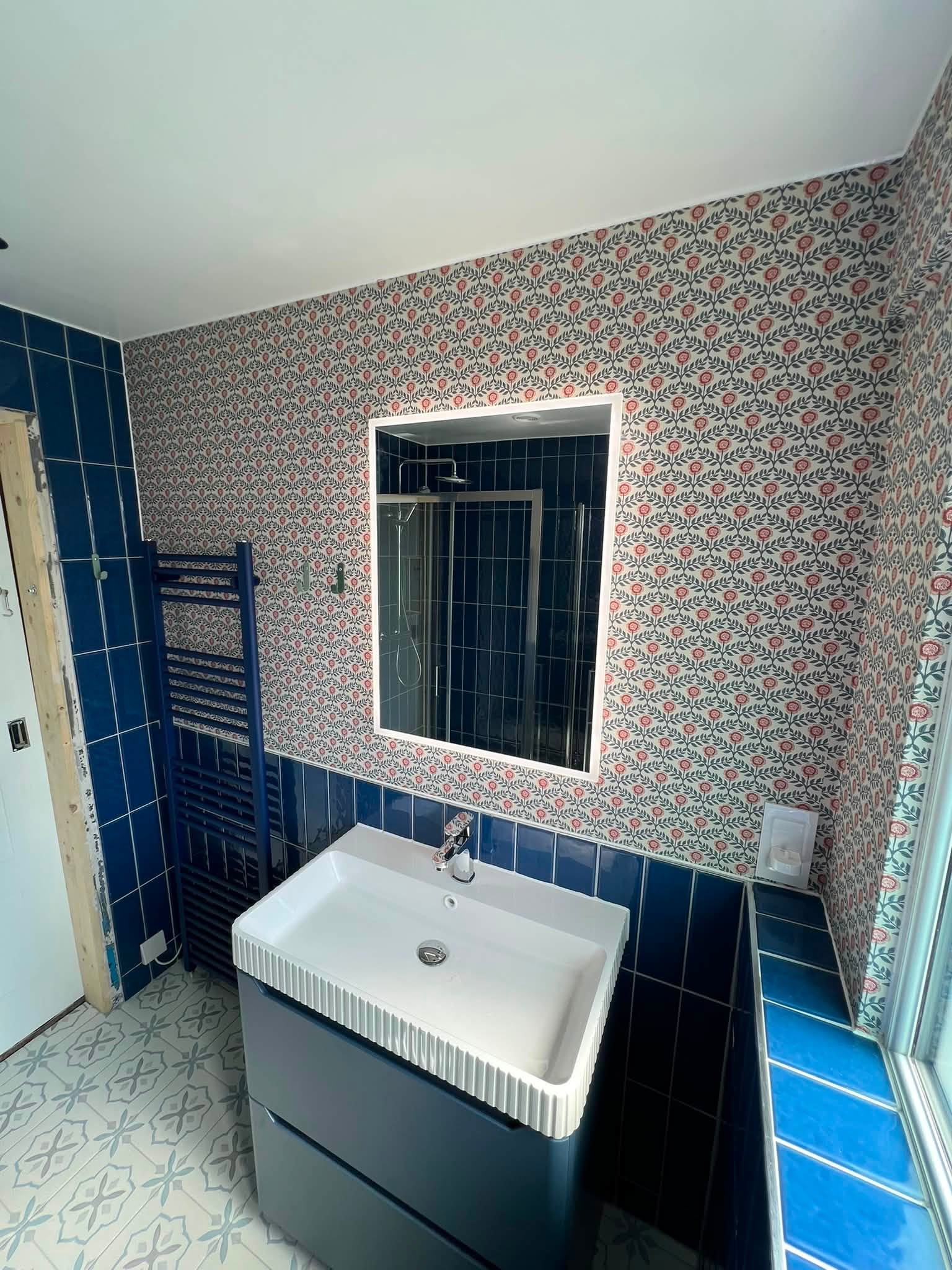 Blue-tiled bathroom renovation with vanity, patterned wallpaper and mirror