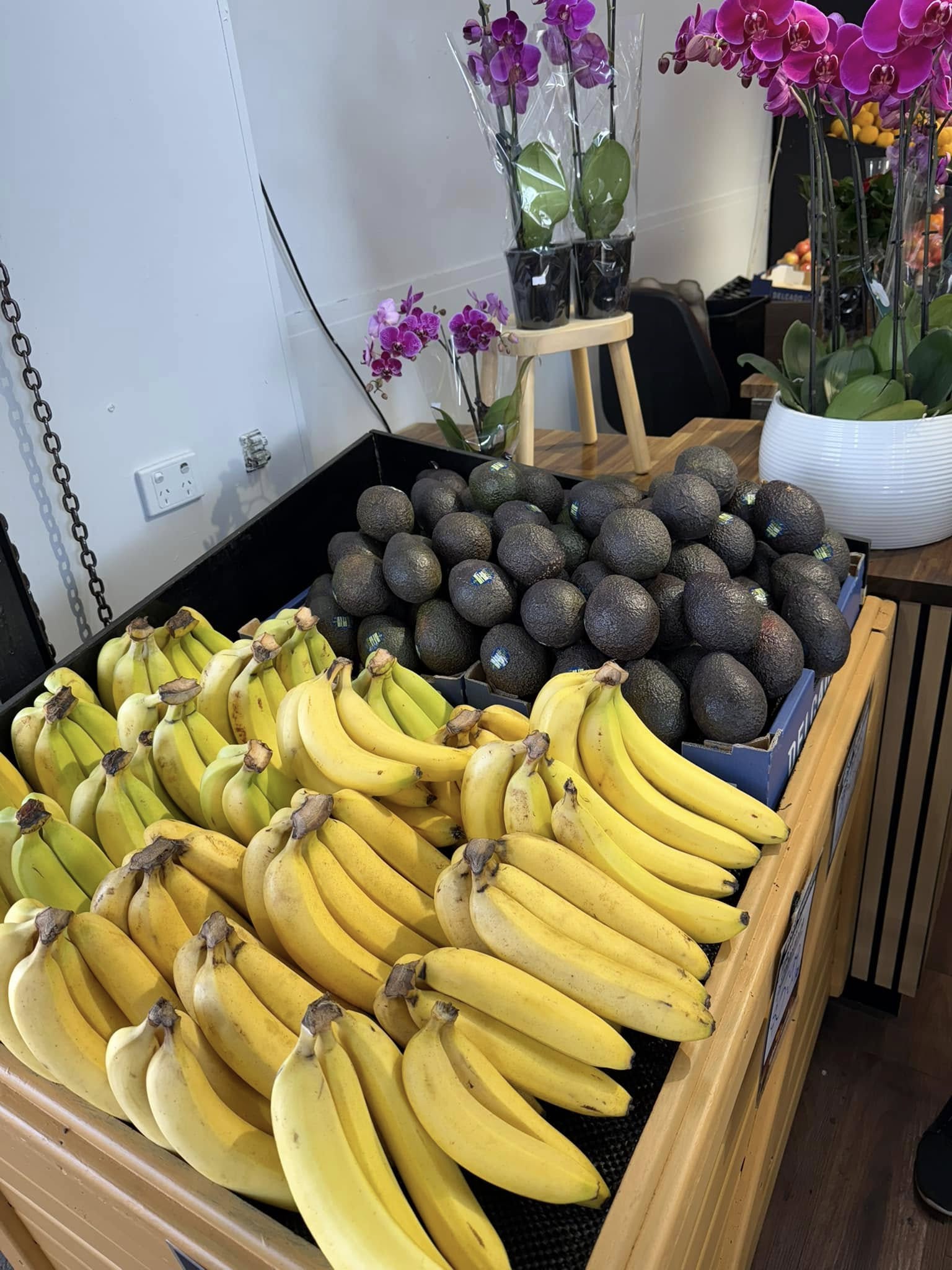 Fresh bananas and avocados displayed in wooden crates with orchid flowers