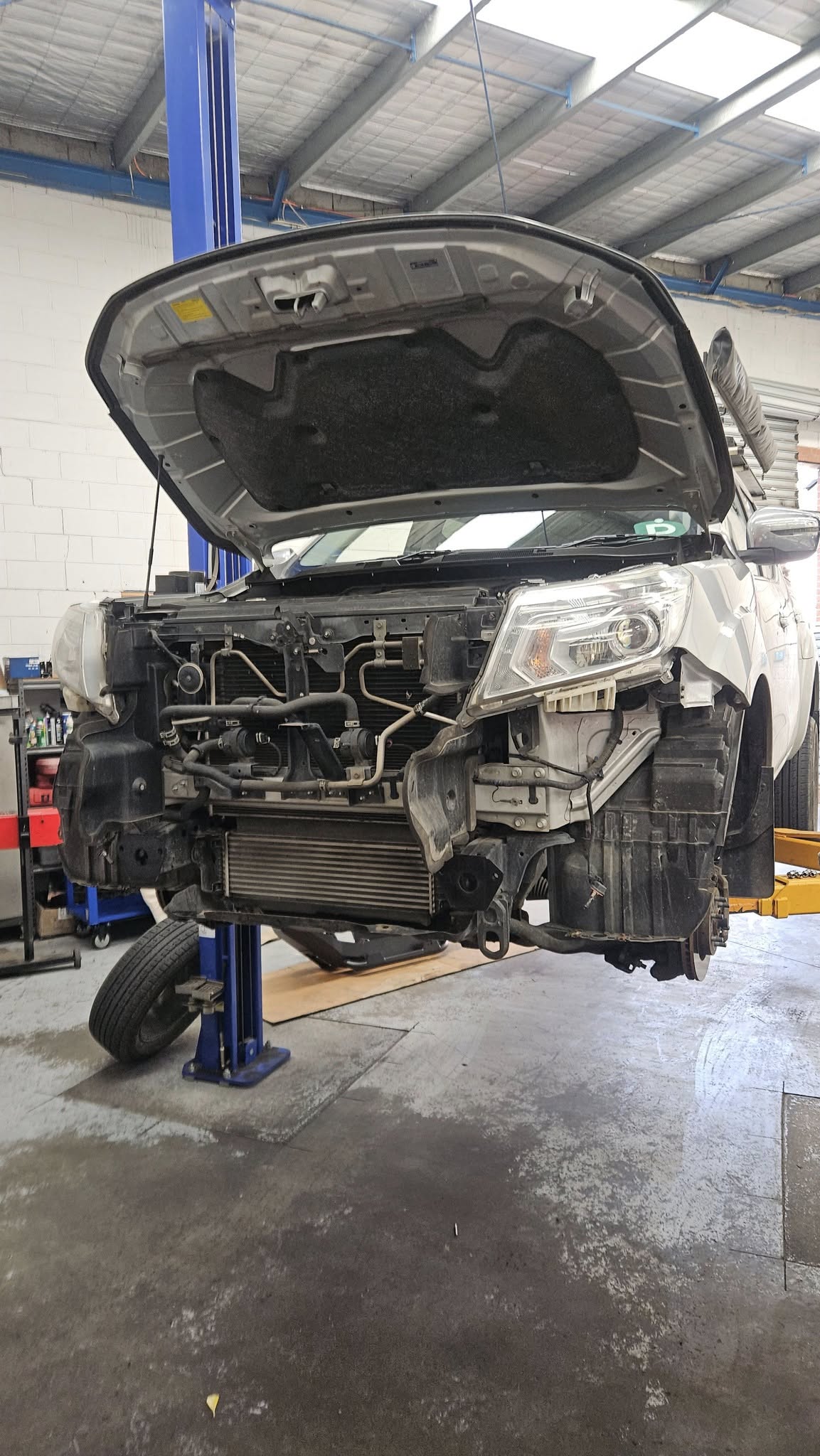 Vehicle on hoist with bonnet open undergoing mechanical repair