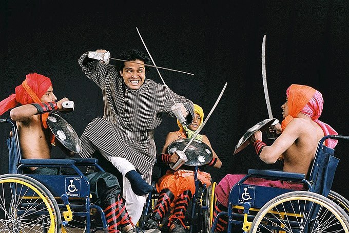 Wheelchair-using performers with swords at a vibrant artistic performance