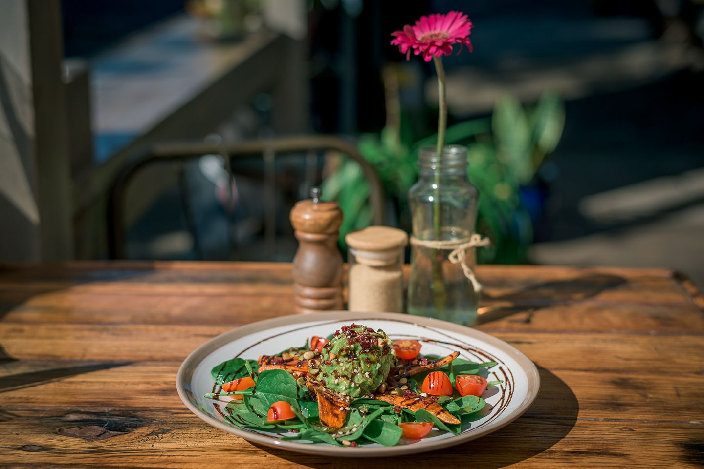 Fresh avocado brunch dish on a white ceramic plate with cherry tomatoes and spinach on a rustic wooden table