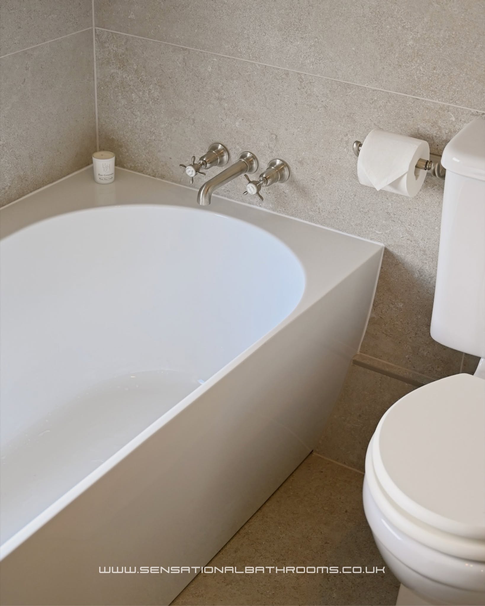 Clean stone-tiled bathroom with freestanding bath, wall-mounted taps and classic toilet