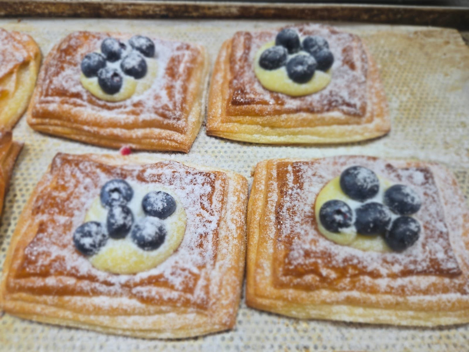 Blueberry custard Danish pastries dusted with icing sugar on a baking sheet