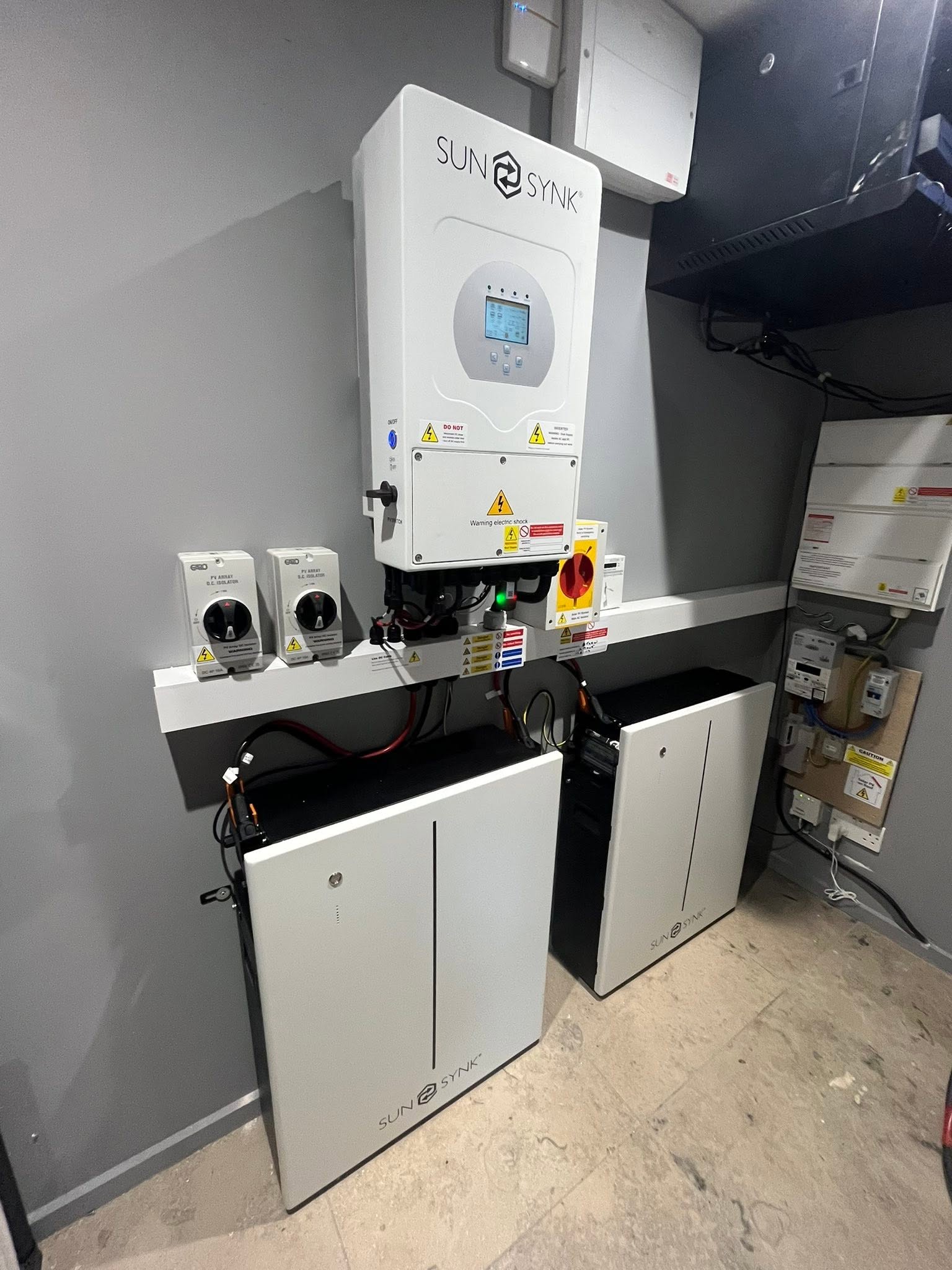 Wall-mounted solar hybrid inverter with two battery units and isolators installed in a utility room