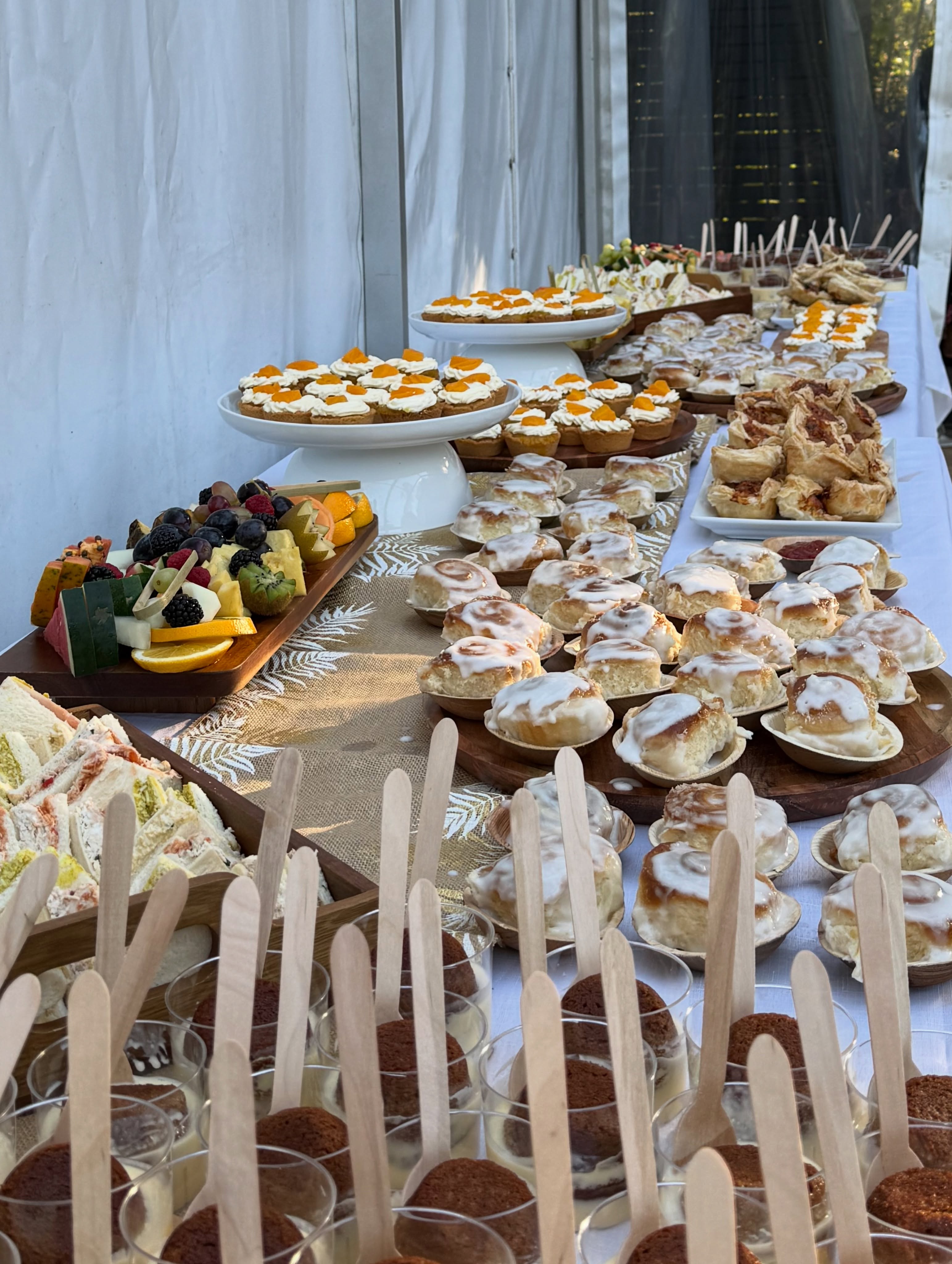 A beautiful event catering spread featuring cinnamon rolls, cupcakes, pastries and fresh fruit at a Lenaya Baked Goods event
