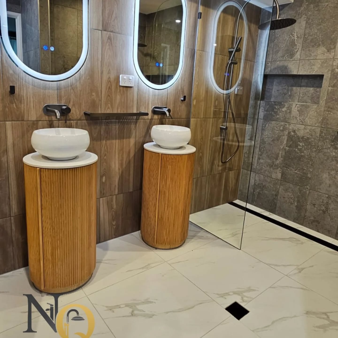 Double vanity bathroom with timber pedestal sinks, oval LED mirrors and marble floor tiles